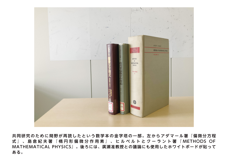 共同研究のために間野が再読したという数学本の金字塔の一部。左からアダマール著『偏微分方程式』、島倉紀夫著『楕円形偏微分作用素』、ヒルベルトとクーラント著『METHODS OF MATHEMATICAL PHYSICS』。後ろには、廣瀬准教授との議論にも使用したホワイトボードが貼ってある。